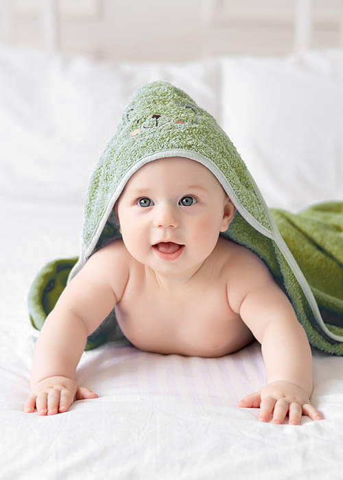 A cute happy laughing baby after a bath is playing on a white bed in a spacious children's room. The child is in a clean and dry towel. Washing, baby hygiene, health and skin care