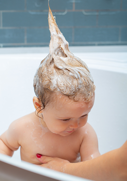 Smiling beautiful baby bathing in shower. Bathing baby. Happy kid with soap foam on head. Child in bathroom play with foam